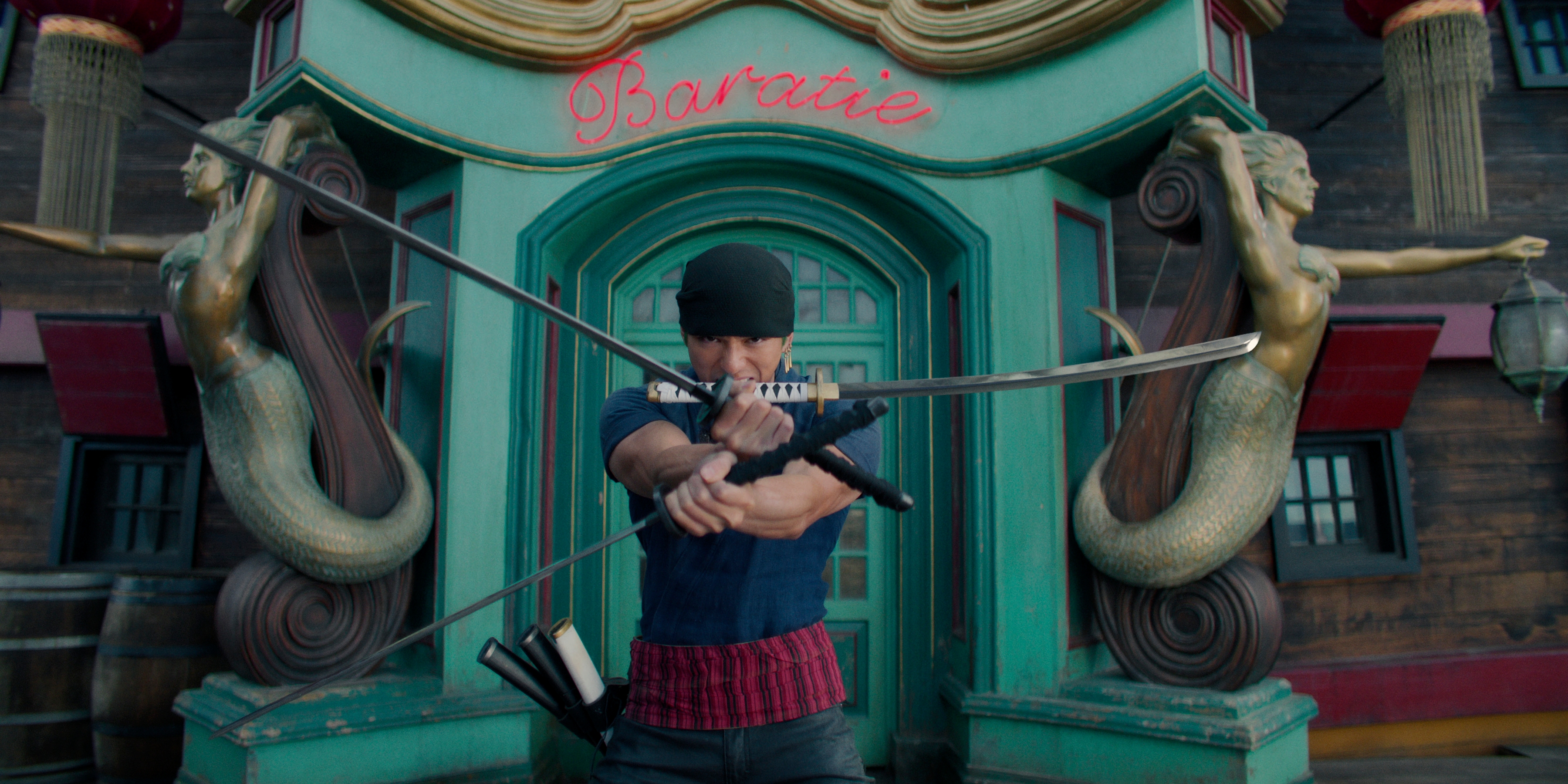 Zoro (Mackenyu) stands in front of the door to the Baratie holding all three of his swords