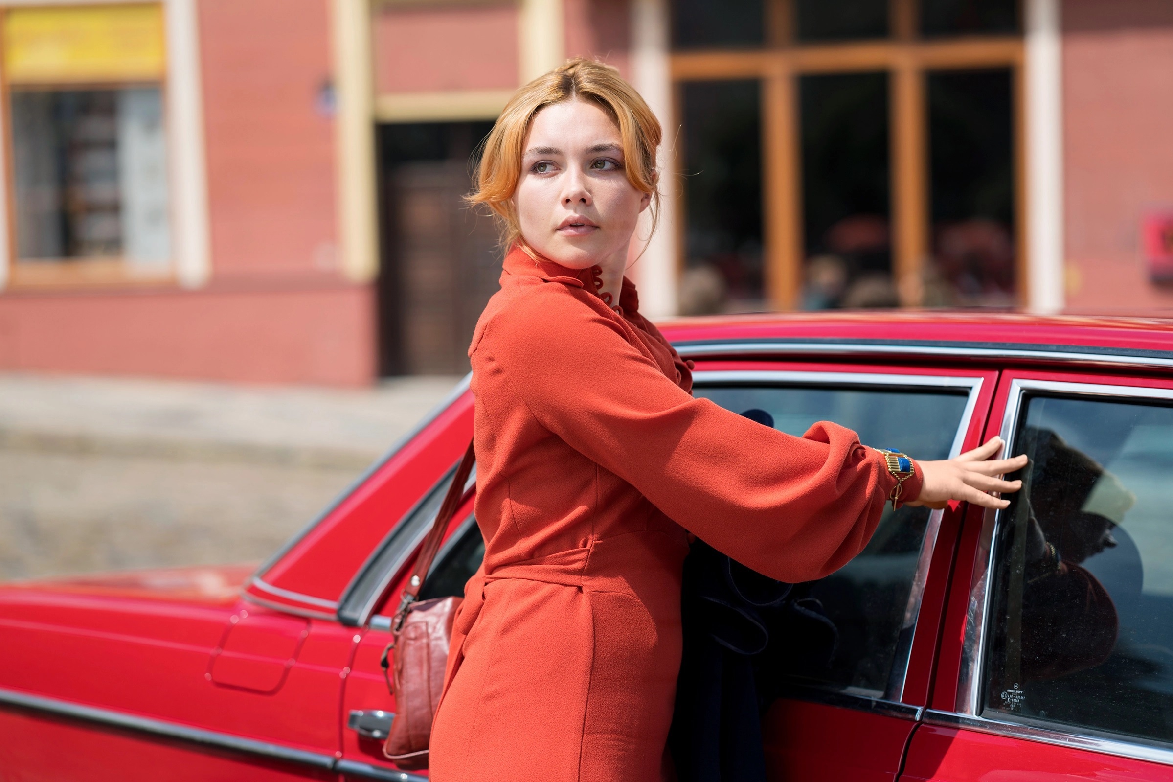 Florence Pugh, wearing red, closes the door of a red car in The Little Drummer Girl.