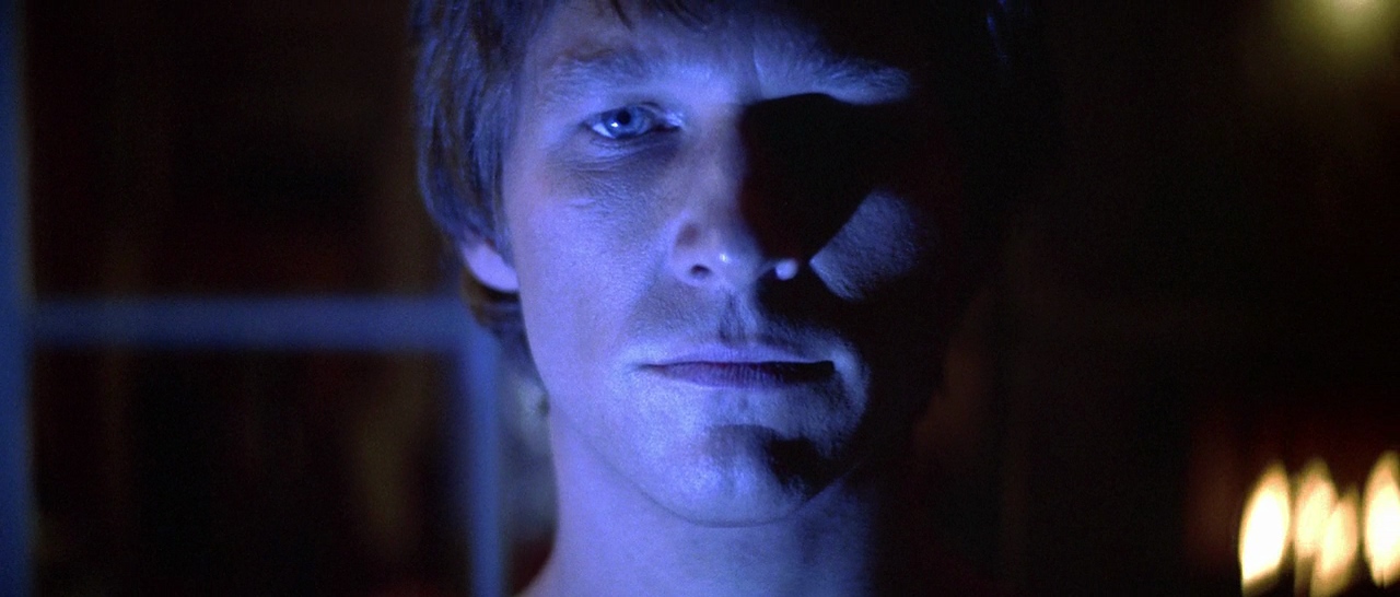 A close-up shot of a man’s stoic face bathed in an unearthly blue light.