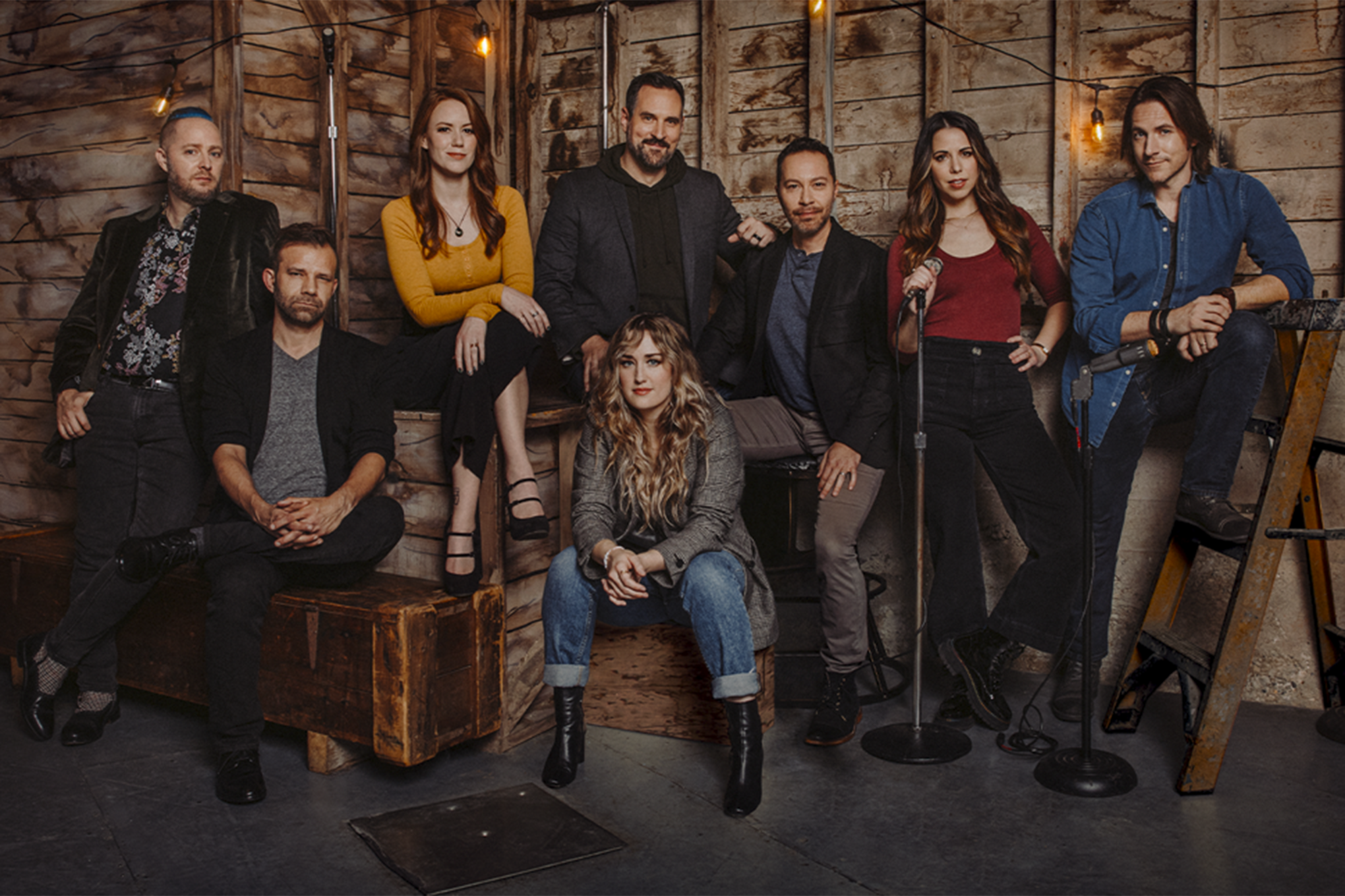 The cast of Critical Role pictured against a rough-hewn wooden wall.